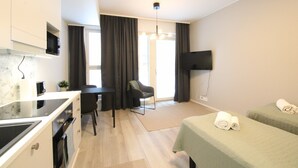 A modern hotel room with a kitchenette, a dining area, a TV, and two beds.