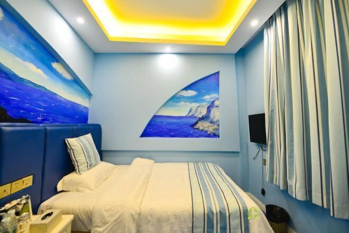 A bedroom with a bed, a nightstand, a wall-mounted TV, and a painting of a seascape.
