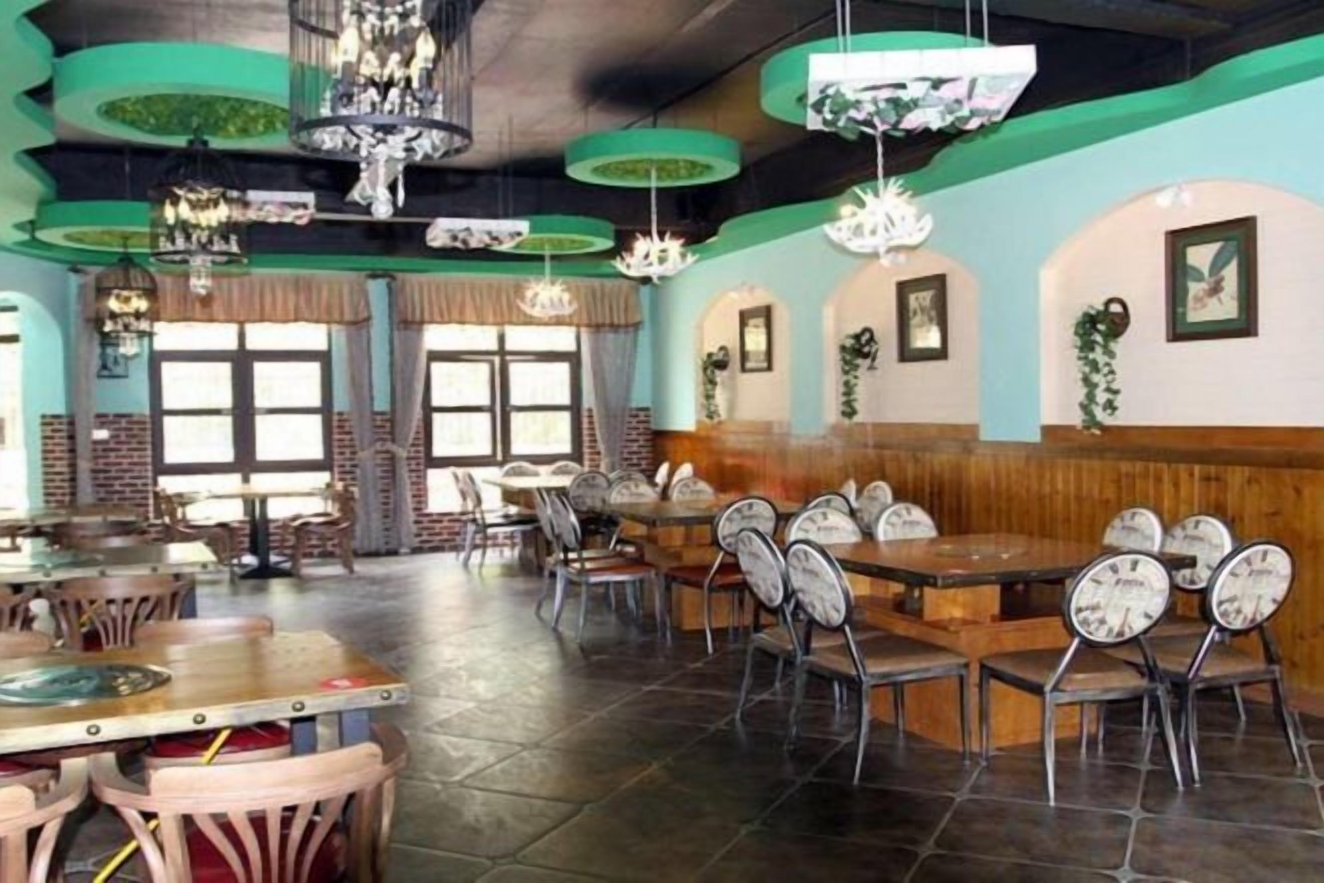 A restaurant interior with multiple dining tables and chairs, large windows, and hanging light fixtures.
