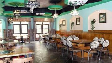 A restaurant interior with multiple dining tables and chairs, large windows, and hanging light fixtures.