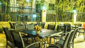 Un patio al aire libre con una mesa y sillas, rodeado de plantas de bambú y un muro de piedra.