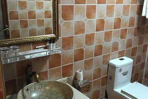 Un baño con lavamanos de granito, espejo con marco decorativo, dispensador de toallas y retrete.
