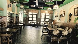Interior de restaurante con paredes de ladrillo, varias mesas y sillas, lámparas colgantes y ventanas amplias.