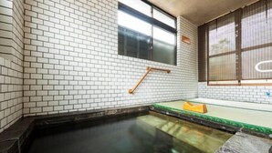 Un onsen japonés tradicional con un muro de azulejos, una escalera de madera y una plataforma de cristal.