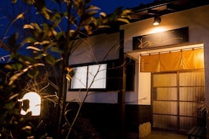 A modern building with a large illuminated window, a sign with a name, and a traditional gate. - Yufuin Wasaku (Yufu)
