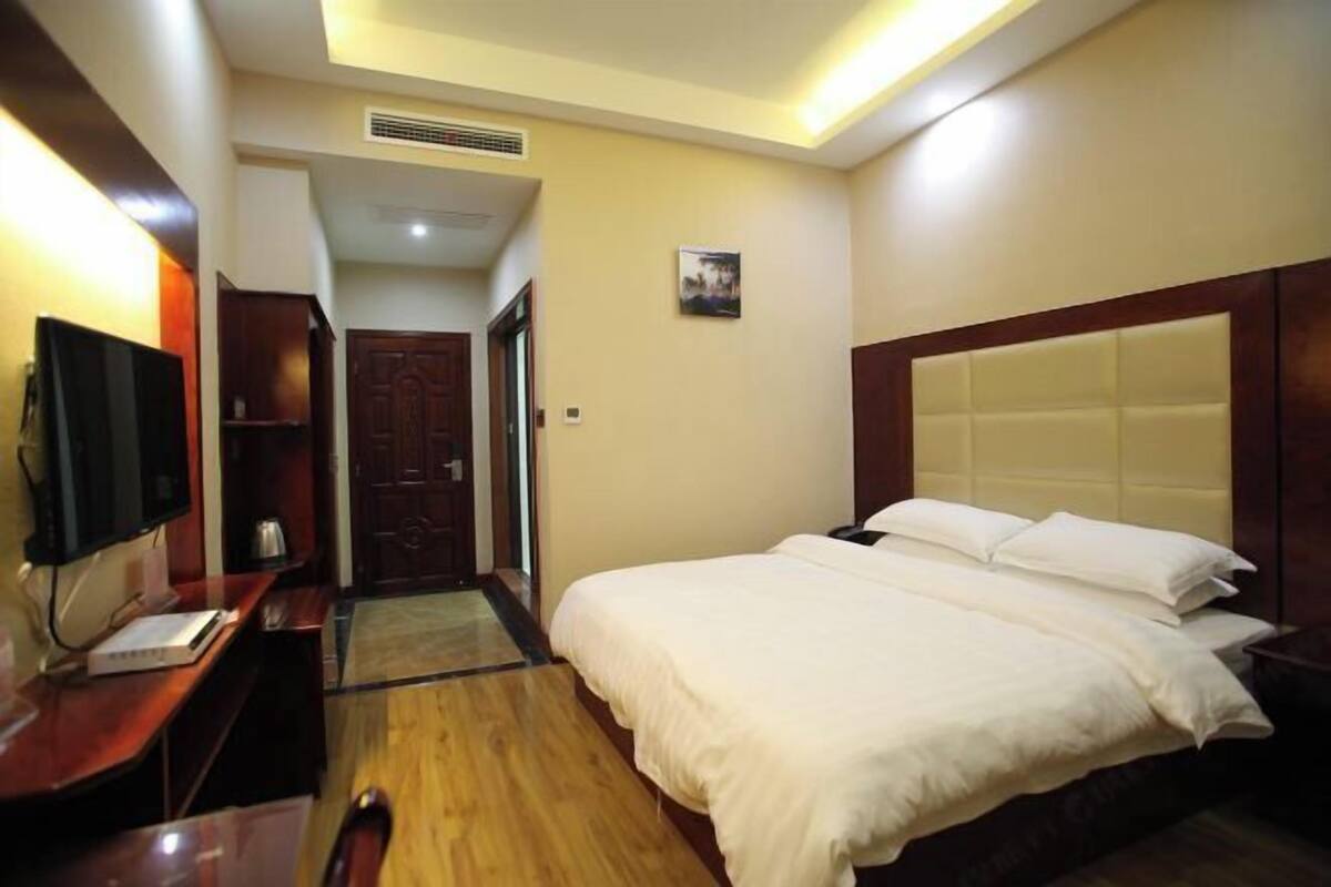 A hotel room with a wooden bed, a desk with a computer, a television, and a door leading to another room.