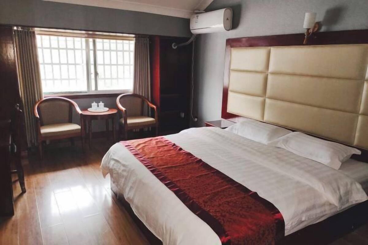 A hotel room with a large bed, a small table with chairs, and a window with curtains.