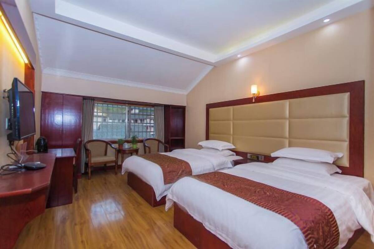 A hotel room with two beds, a desk with a computer, a TV, and a window with curtains.