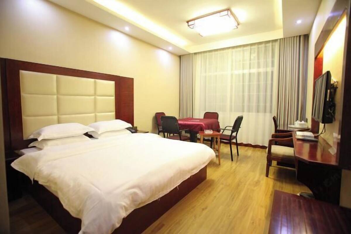 A hotel room with a large bed, a desk, a chair, and a TV.