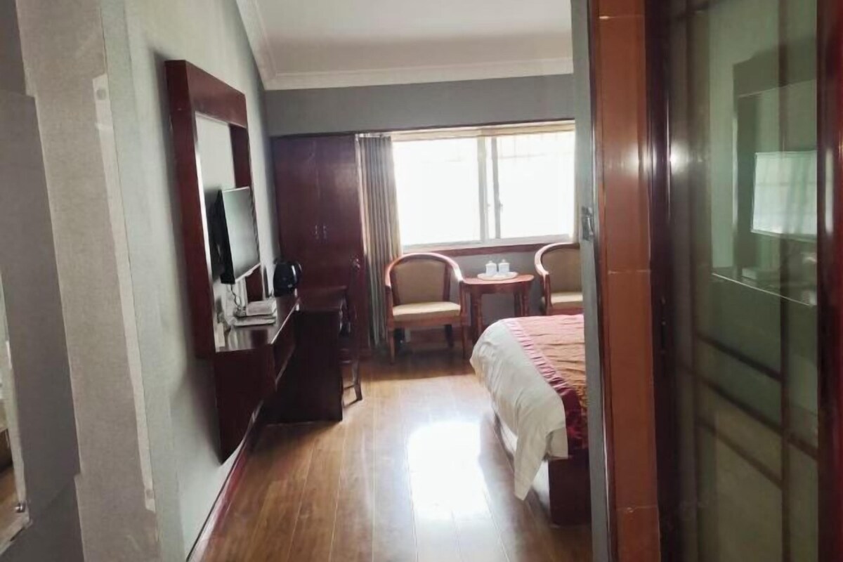 A hotel room with a bed, a desk with a computer, a chair, and a small table with a lamp.