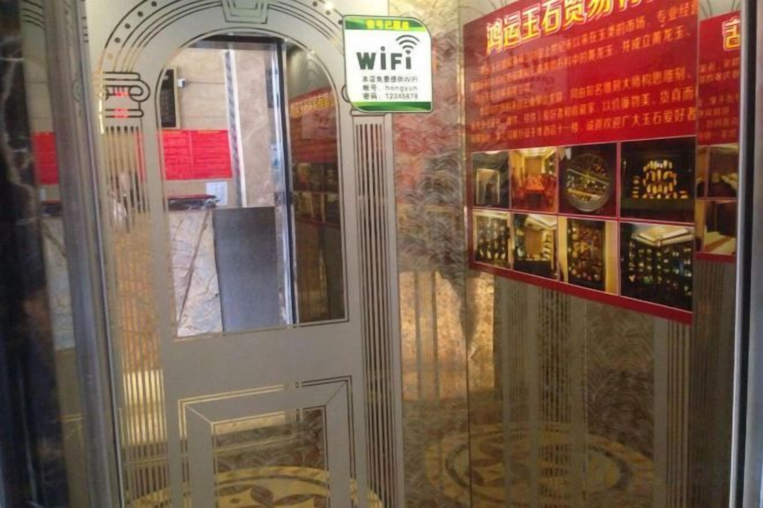Entrada de hotel con un letrero de WiFi, un cartel informativo rojo y una puerta de cristal.