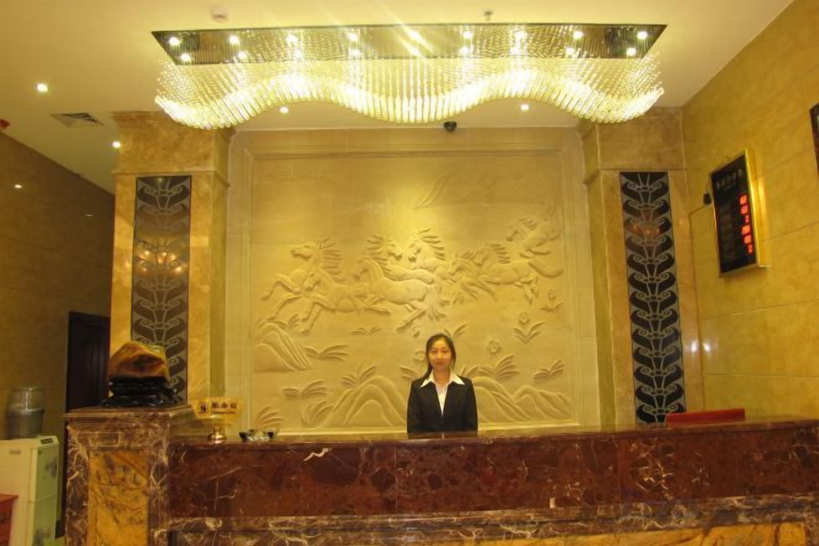 A reception desk with a marble counter, a receptionist, and a decorative wall with relief art.
