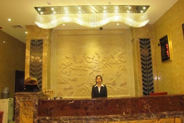 A reception desk with a marble counter, a receptionist, and a decorative wall with relief art.