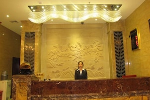 Balcão de recepção com bancada de mármore, recepcionista e parede decorativa com relevos.