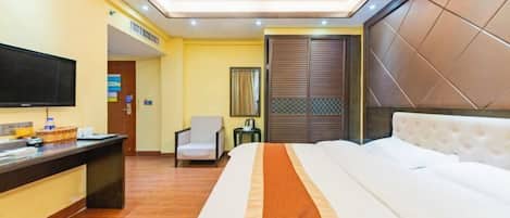 A hotel room with a bed, a desk with a flat-screen TV, a chair, and a window with blinds.
