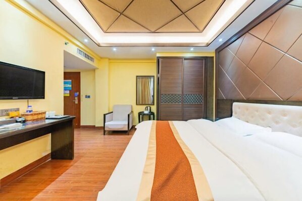 A hotel room with a bed, a desk with a flat-screen TV, a chair, and a window with blinds. - Hongyun Hotel (Hezhou)