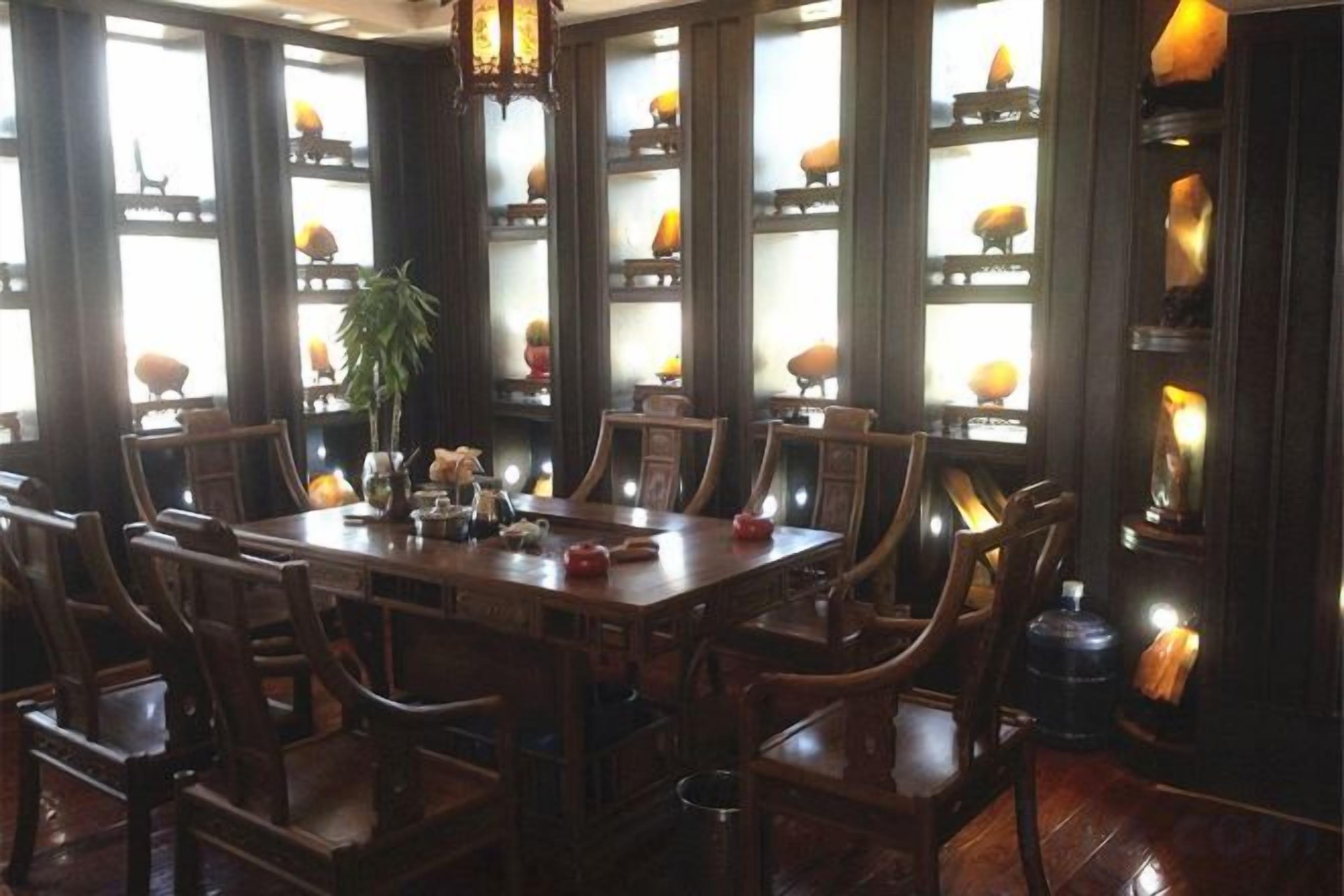 A dining area with a large wooden table surrounded by chairs, large windows with decorative elements, and a chandelier.