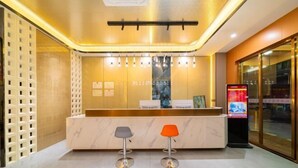 Un espace d’accueil doté d’un comptoir en marbre, de deux tabourets, d’un panneau d’affichage numérique et d’un mur en verre.