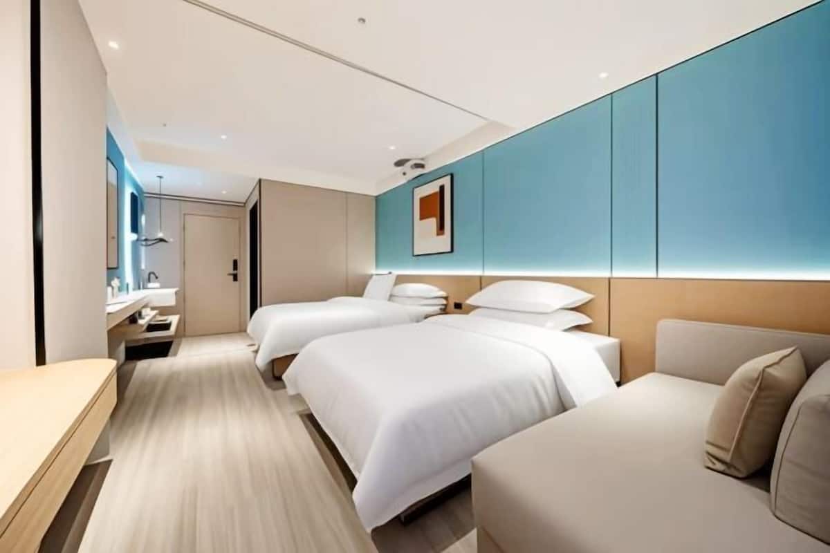 A modern hotel room with two beds, a sofa, a desk, and a bathroom.