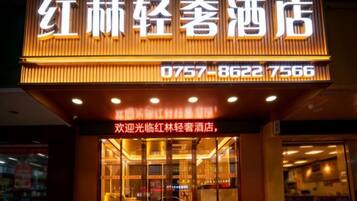 A hotel with a prominent illuminated signboard displaying the name and contact number.