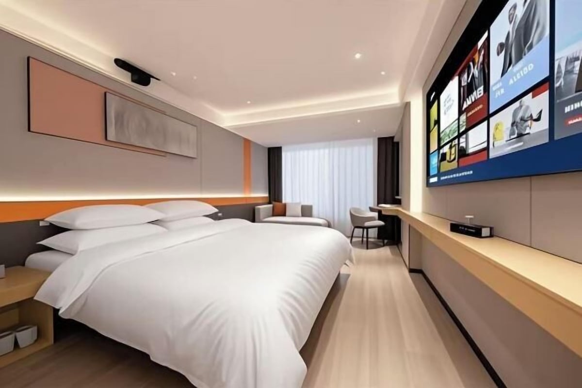 A modern hotel room with a large bed, a desk, and a TV mounted on the wall.