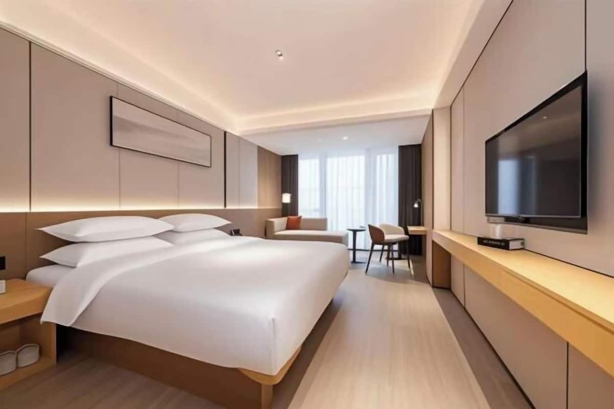 A modern hotel room with a large bed, a desk, and a TV mounted on the wall.