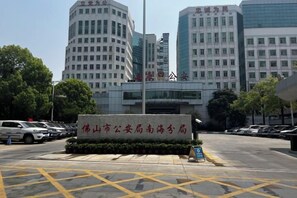 A building with a sign in front, surrounded by other buildings and parked cars. - Honglin Hotel (Foshan)