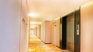 Un couloir d’hôtel avec un tapis à motifs, des murs en bois et une rangée d’ascenseurs.