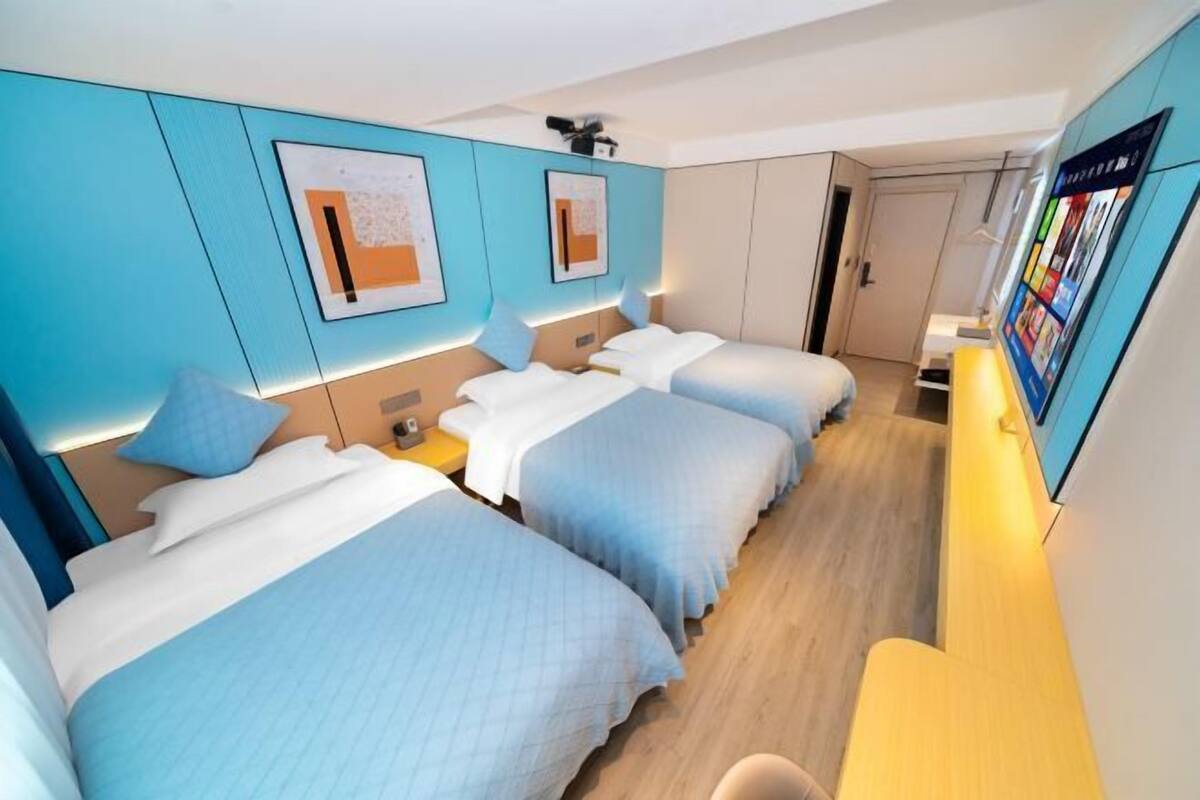 A hotel room with three beds, a desk, and a TV.