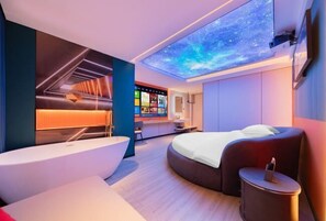 A modern hotel room with a curved bed, a large window, a ceiling projection, and a wall-mounted TV. - Honglin Hotel (Foshan)
