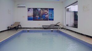 An indoor swimming pool with a tiled floor, two lounge chairs, and a wall-mounted air conditioner. - 1bed - Balcony - Pool - Gym - Spa (Lekki)