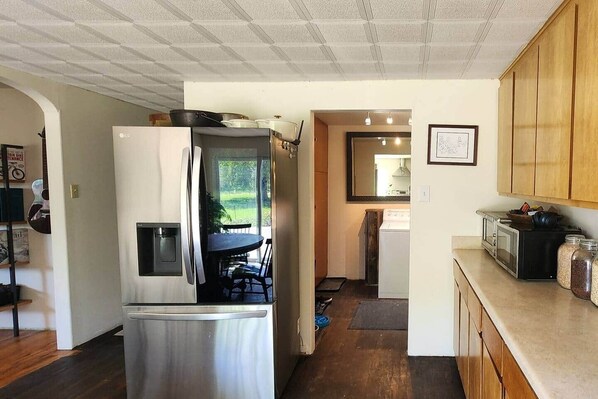 A compact kitchen with a refrigerator, microwave, and stove. There is a dining area with a table and chairs, and a view of the outdoors through a door.