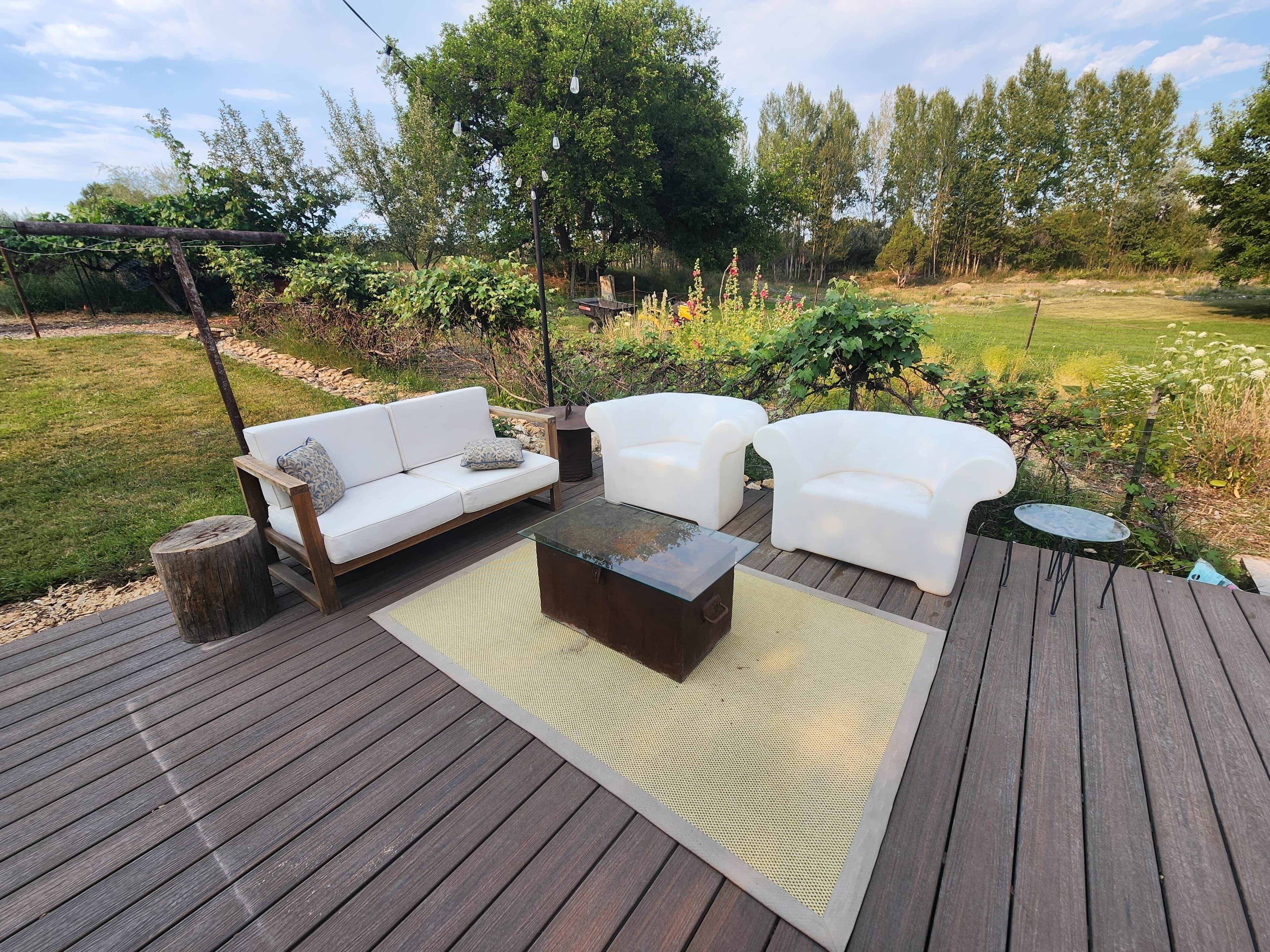 Una terraza al aire libre con piso de madera, sofás blancos y una mesa de centro de vidrio.