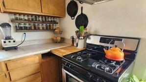 A kitchen with wooden cabinets, a stove, a blender, and a pot on the counter.