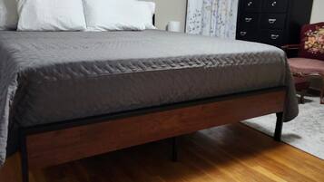 Una camera da letto con un letto, pavimento in legno, una cassettiera nera e una tenda floreale.