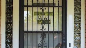 Un portail en métal noir orné d’éléments décoratifs et doté d’un panneau en verre, intégré dans un cadre de porte blanc, avec un paillasson devant.