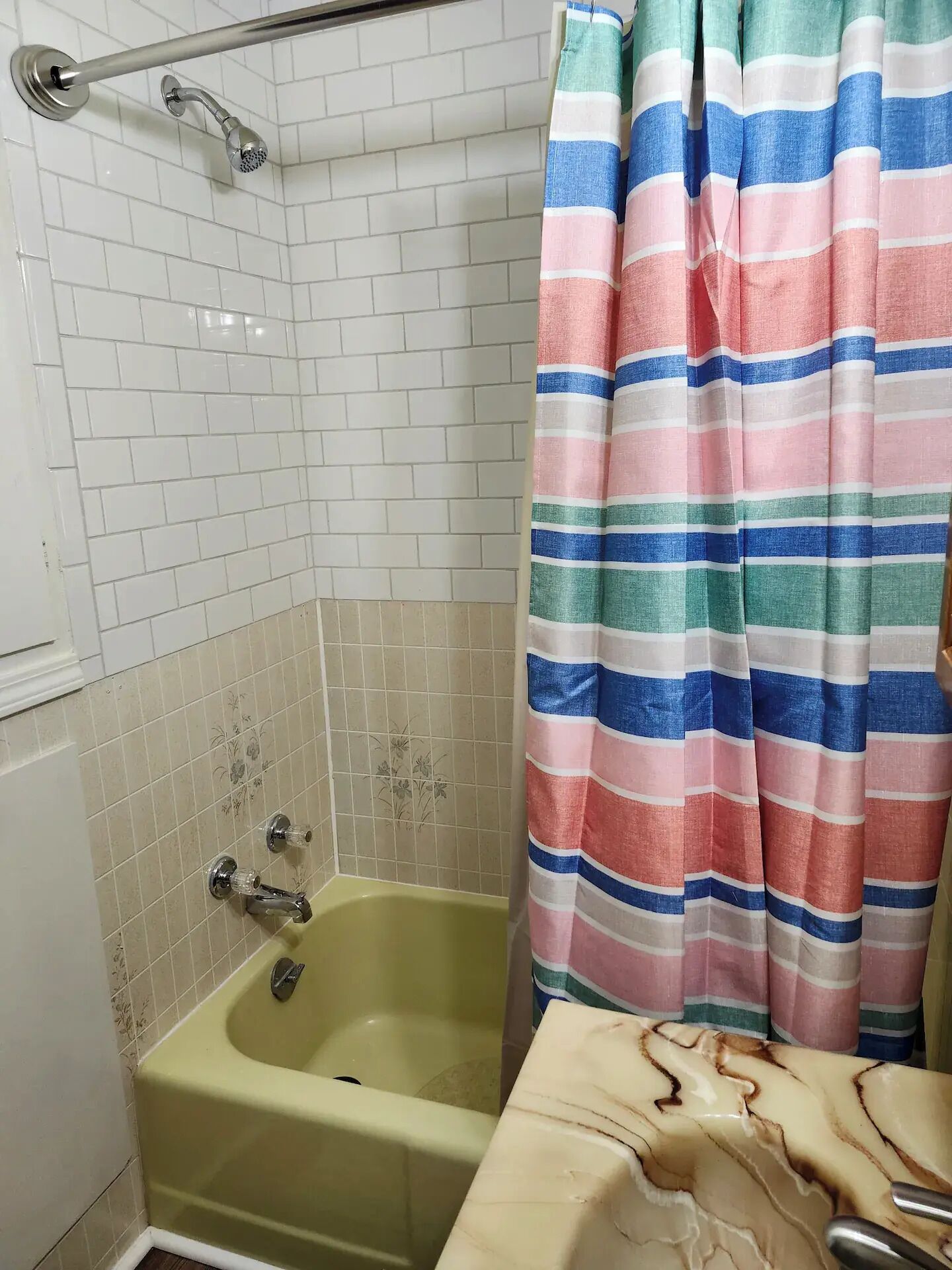 Een badkamer met een bad, een douche met een metalen handgreep en een gestreept douchegordijn.