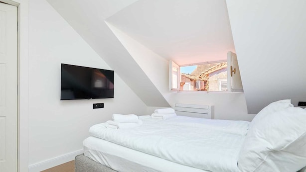 A bedroom with a bed, a flat-screen TV mounted on the wall, and a window with a view of a building outside. - 3 TUDISI LUX SUITES by DOMINIUM deluxe double room (loft) (Dubrovnik)