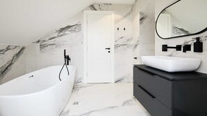 A modern bathroom with a freestanding bathtub, a white vanity with a large mirror, and marble-patterned walls. - 3 TUDISI LUX SUITES by DOMINIUM deluxe double room (loft) (Dubrovnik)
