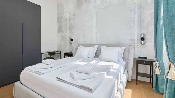 Ein modernes Hotelzimmer mit einem großen Bett, zwei Nachttischen, einem Kleiderschrank und Blick auf die Stadt.