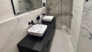 Un baño moderno con dos lavamanos, un espejo grande y una cabina de ducha de cristal.