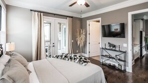 Een slaapkamer met een bed, een plafondventilator, een televisie en een gang naar een keuken.