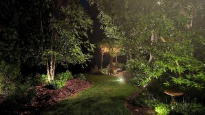 Een goed verlichte tuin met een pad, bomen en een zitgedeelte.