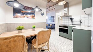 A modern kitchen with a dining area, featuring a wooden table, wicker chairs, and pendant lighting.