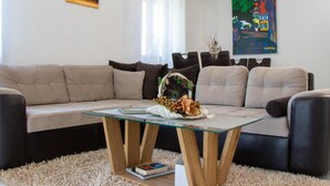 A living room with a beige sectional sofa, a glass coffee table, and a painting on the wall. - Authentic Dalmatian Treasure Homes - House Stone (Orebic)