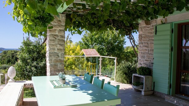 Un espace extérieur aménagé pour les repas, avec une table et des chaises, une pergola couverte de plantes grimpantes, des piliers en pierre et une vue sur le paysage.