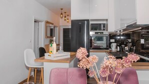 Une cuisine moderne dotée d’un îlot central, de meubles blancs, d’appareils électroménagers en acier inoxydable et d’un coin repas avec des chaises roses.