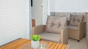 Un espace de détente extérieur accueillant, avec des fauteuils en osier et une table en bois, agrémenté d’une petite plante en pot et d’un chandelier en verre.