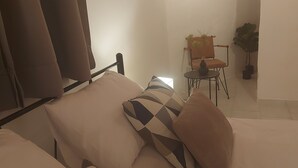 Une chambre à coucher avec un lit, des oreillers, une chaise et une petite table sur laquelle se trouve un vase.