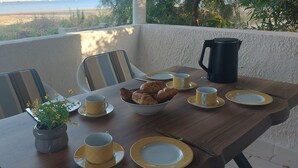 Une table à manger dressée avec des assiettes, des tasses, un bol de croissants, une cafetière et une plante en pot.